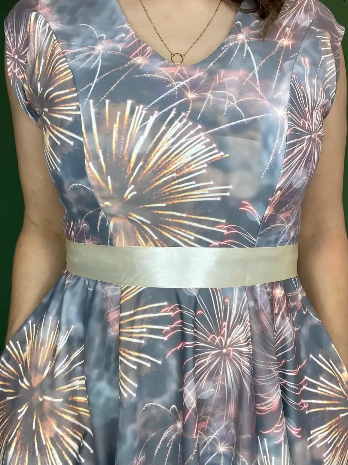 A woman wears a dress with a fireworks pattern and a light-colored ribbon belt.