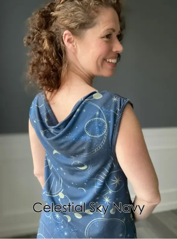 A woman in a blue celestial print top with a cowl neck smiles over her shoulder.