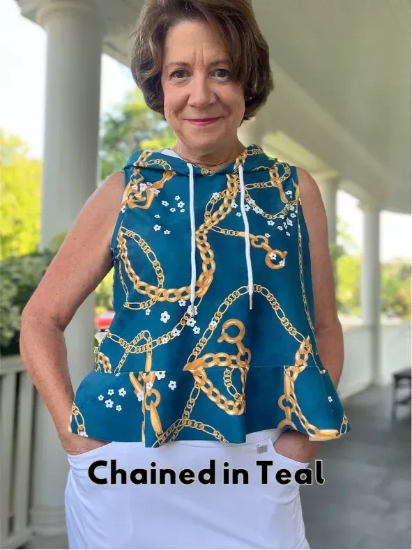 A woman models a teal sleeveless hoodie with a gold chain and white flower pattern.