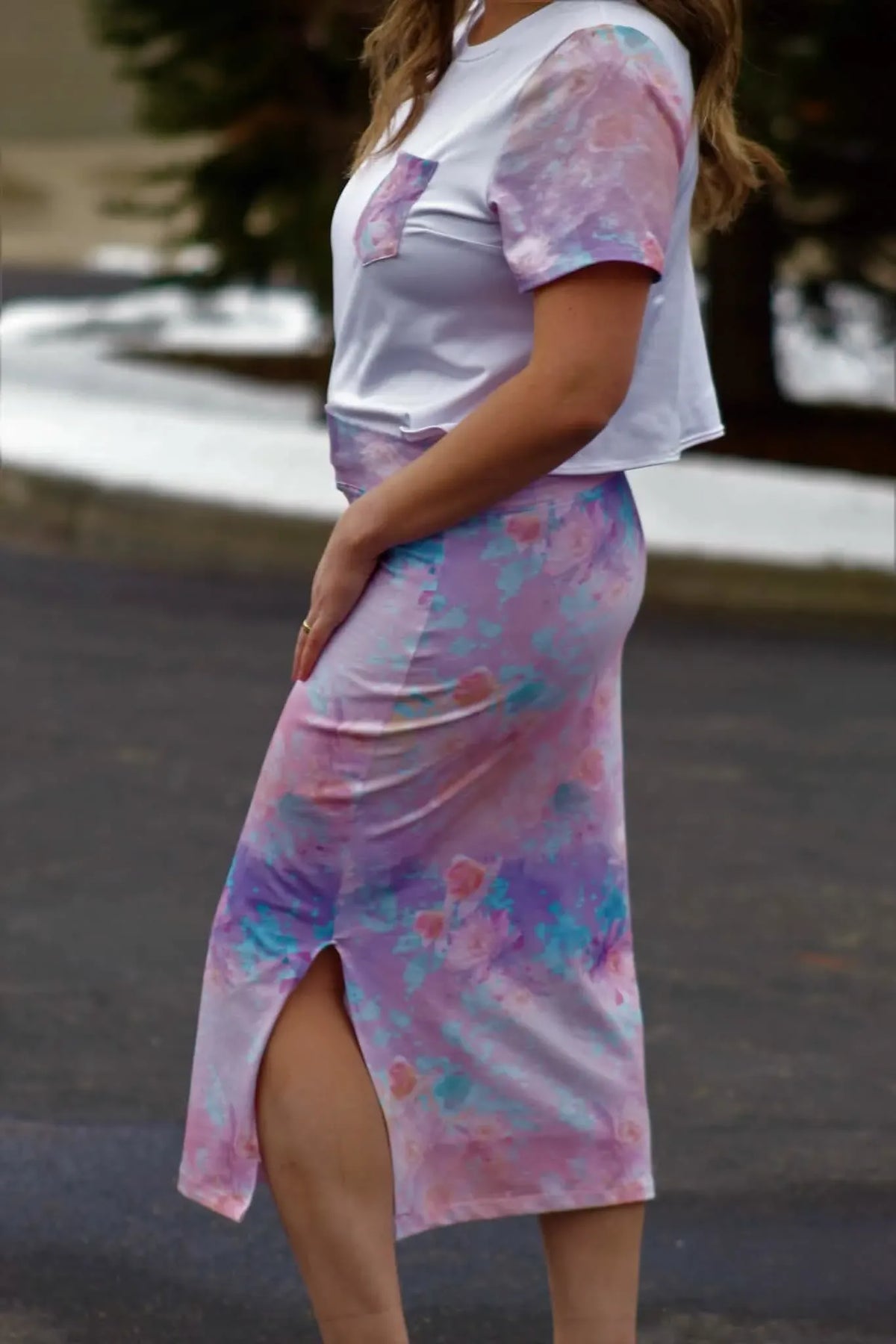 A woman wears a white top with purple floral sleeves and a matching long skirt.