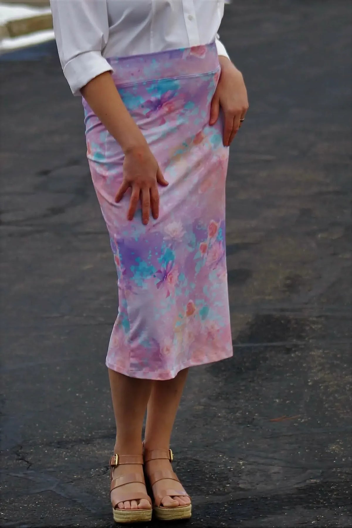 A person wears a purple and blue floral skirt with a white shirt and platform sandals.