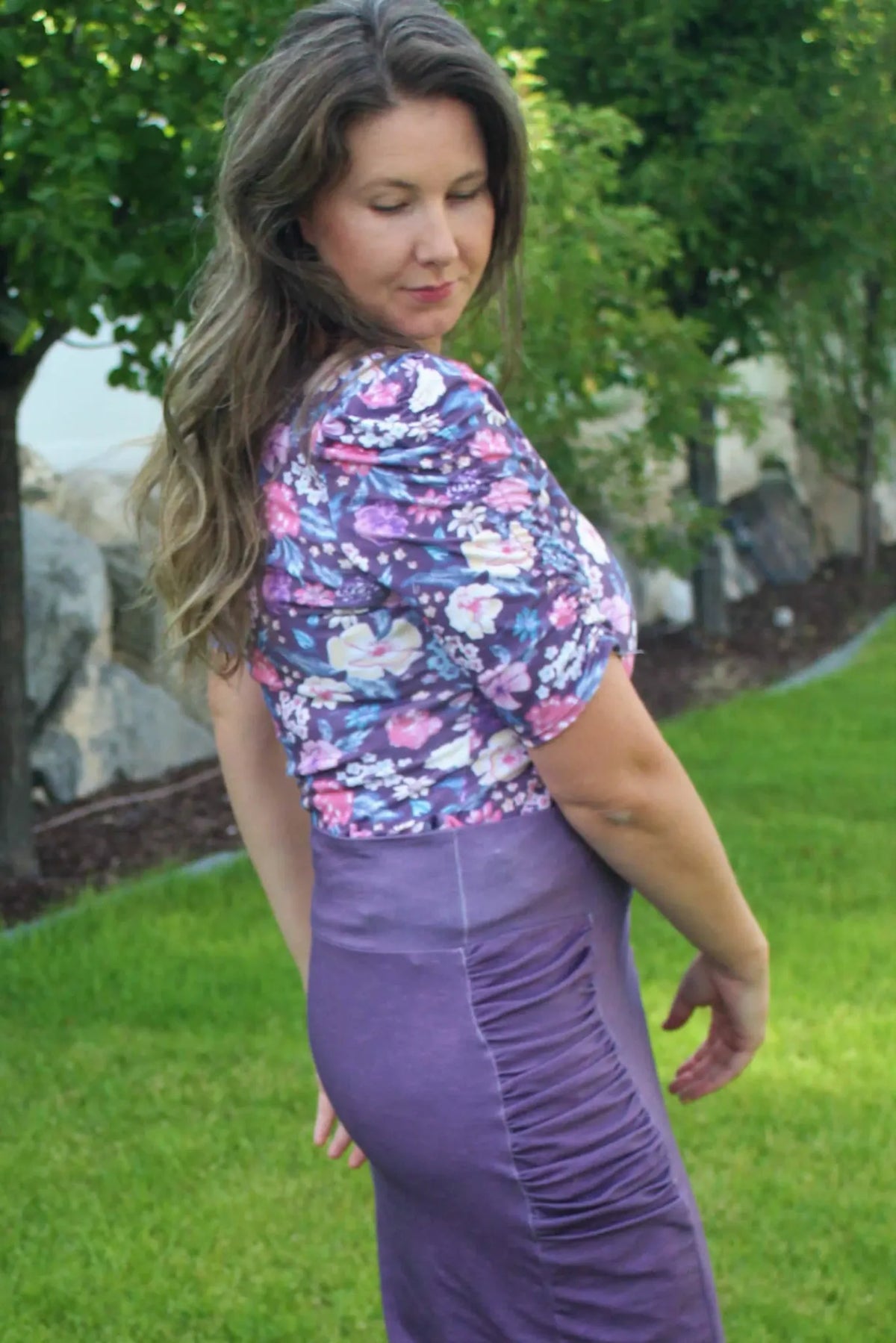 A woman models a floral top and a ruched purple skirt.
