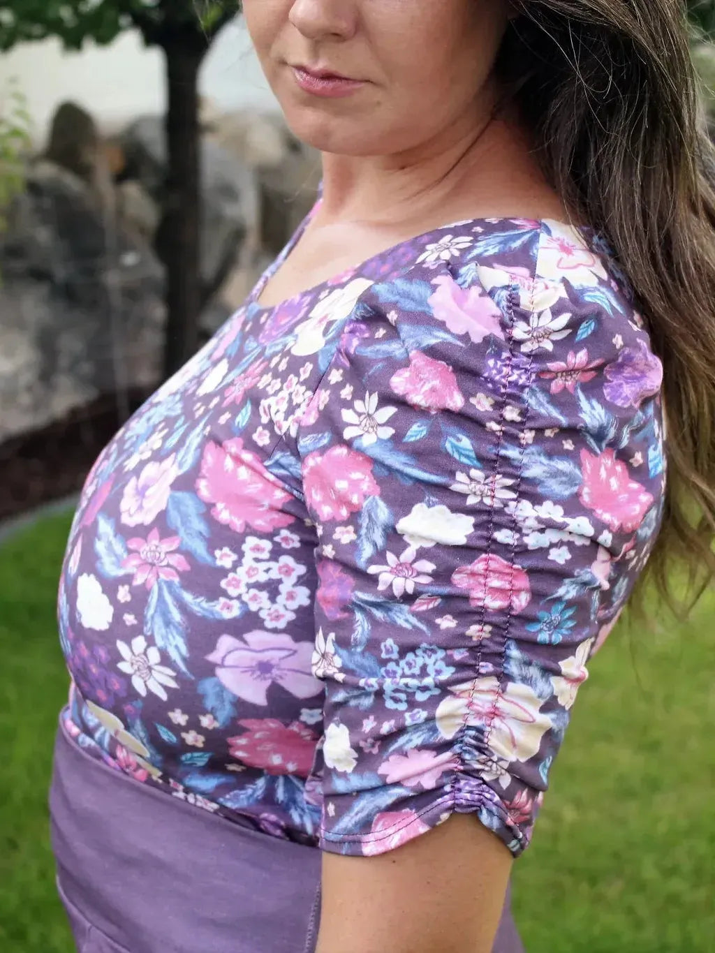 A woman wears a purple floral top with ruched sleeves.