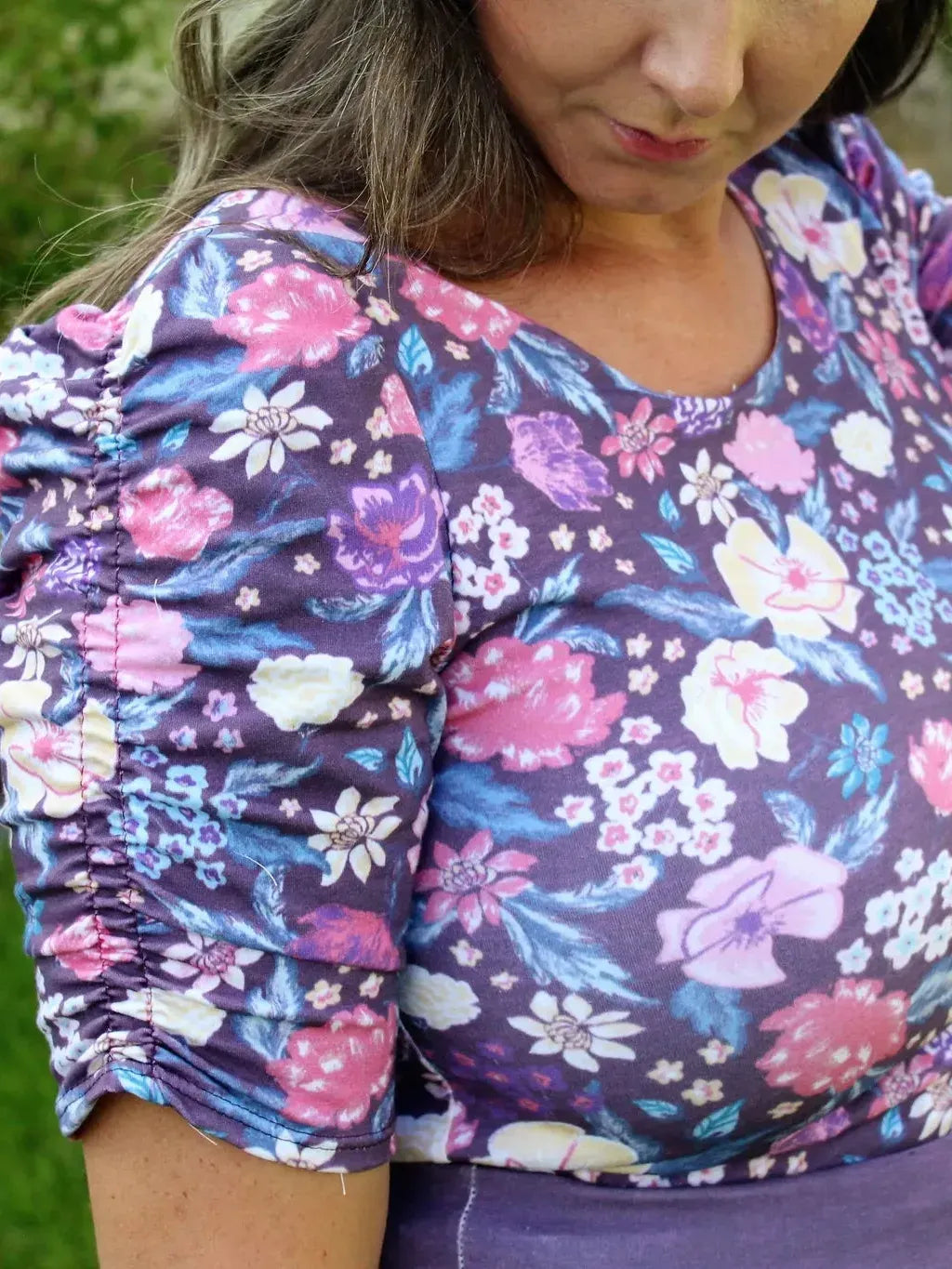 A woman wears a purple floral top with ruched sleeves.