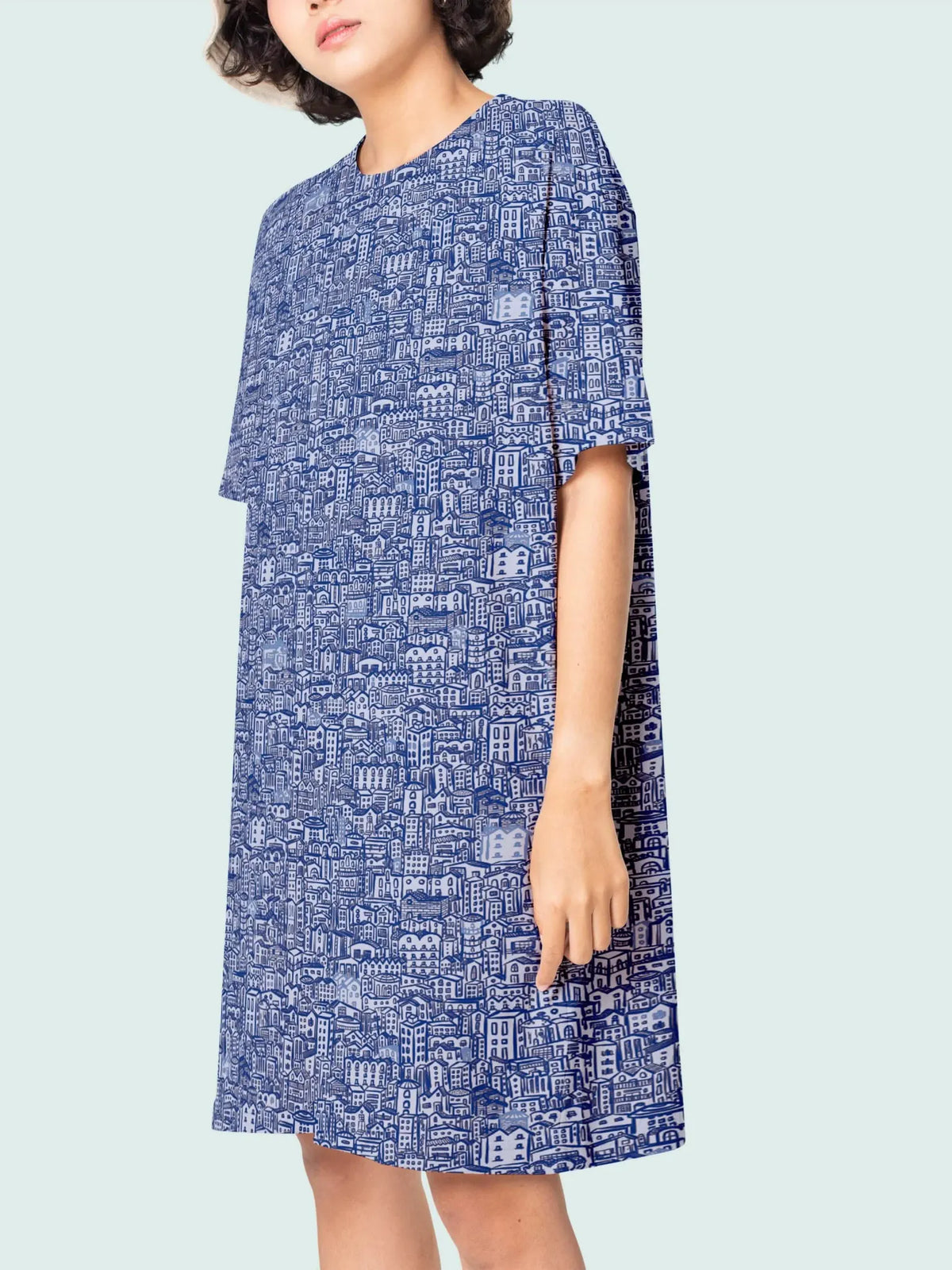 A woman wears a blue dress with a white city illustration pattern.