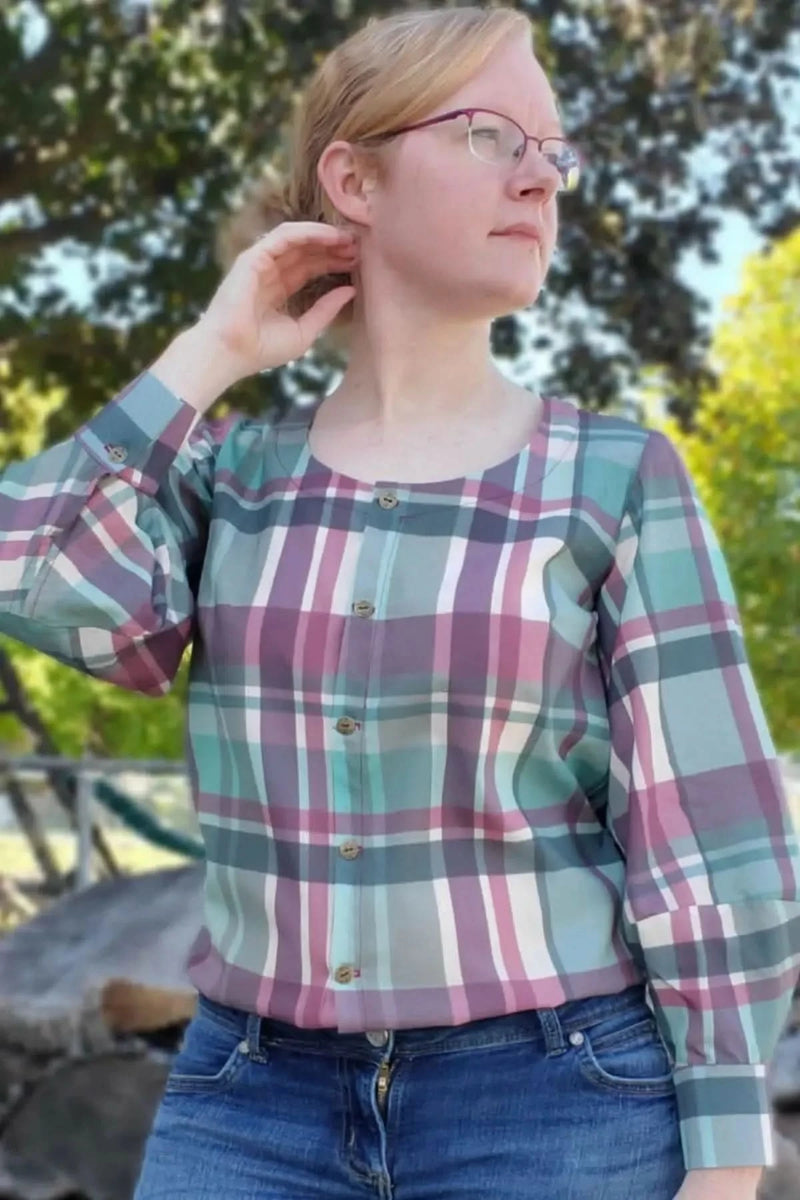 A woman wears a plaid shirt with shades of purple, teal, and white.