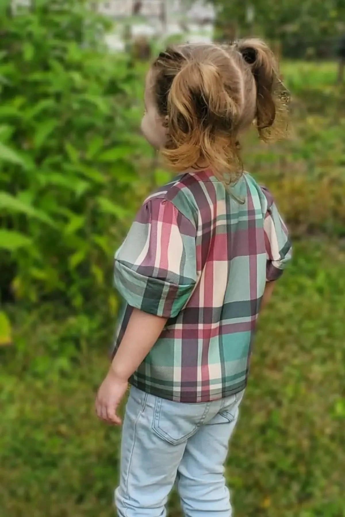 A child from behind wears a plaid shirt with green, pink, and white colors.