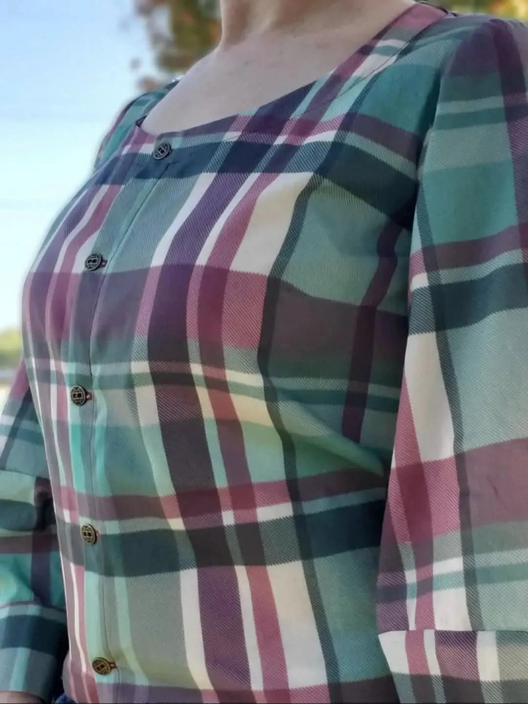 A person wears a plaid shirt with teal, purple, pink, and white colors.