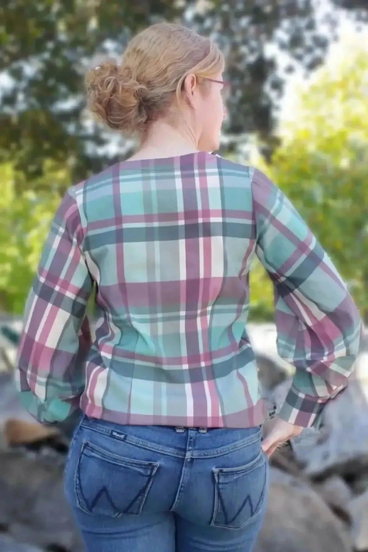 A woman from behind wears a teal and purple plaid shirt and blue jeans.