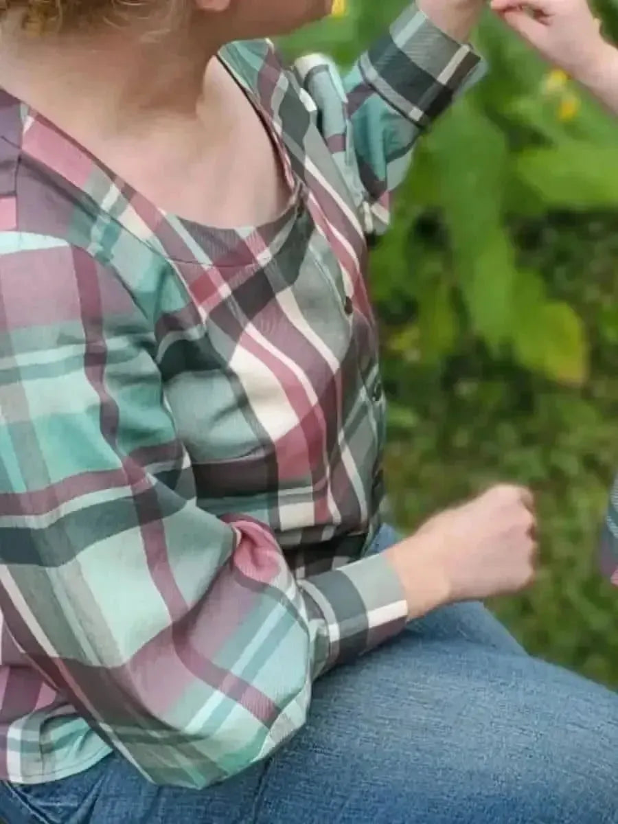 A person wears a teal and purple plaid shirt with blue jeans.