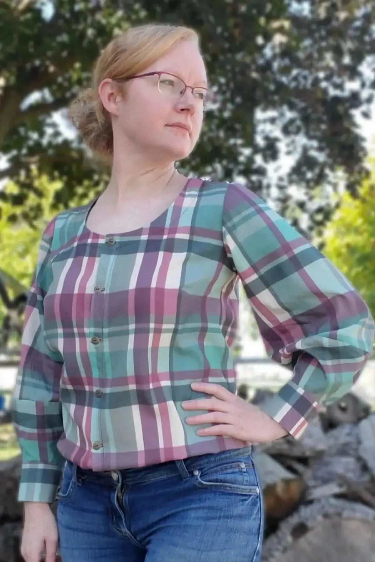 A woman wears a teal and purple plaid button-up shirt with puffed sleeves.