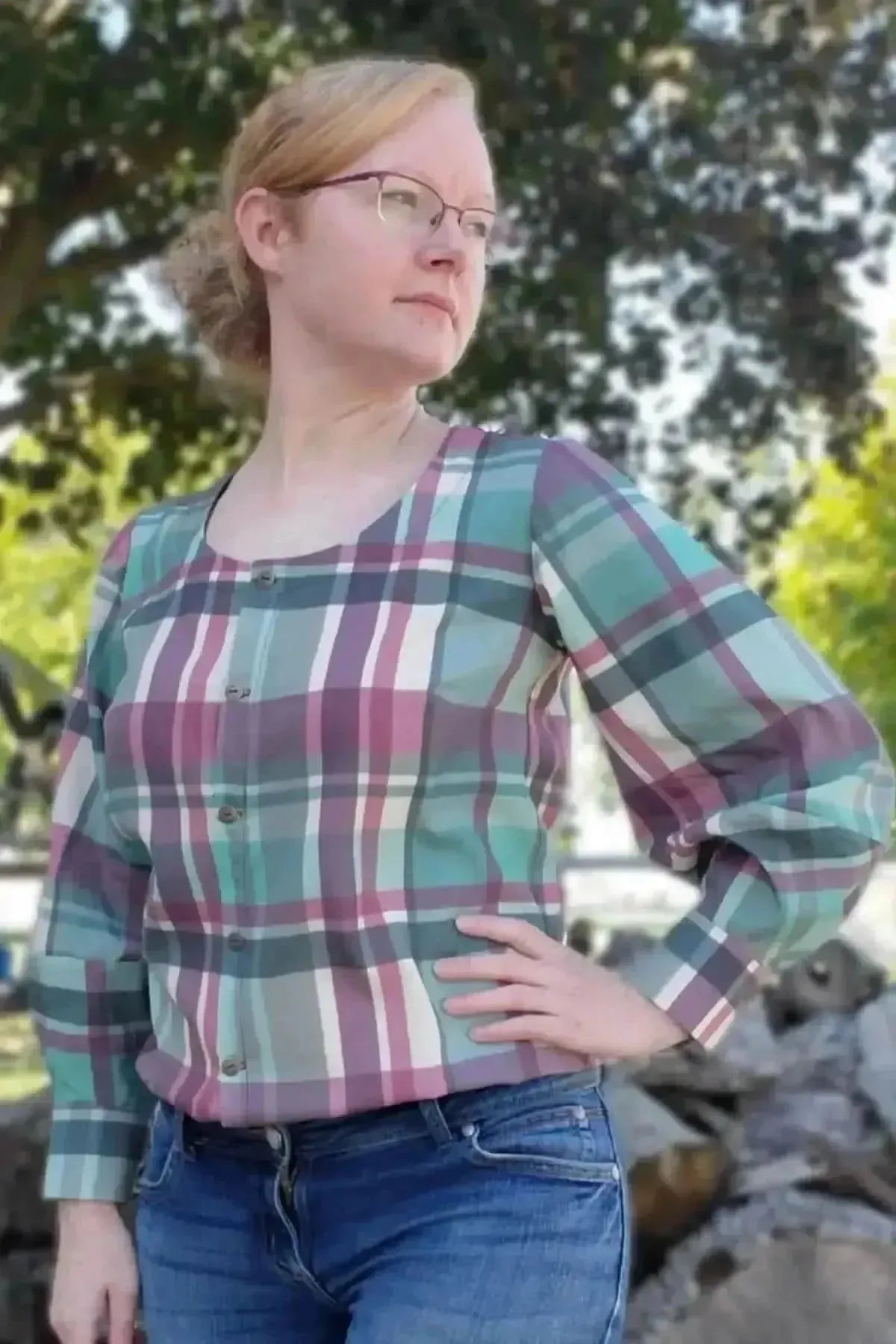 A woman wears a teal and purple plaid button-up shirt with puffed sleeves.