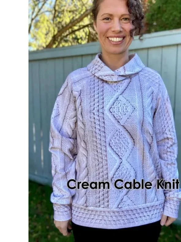 A woman smiles while wearing a cream cable knit sweater with a cowl neck.