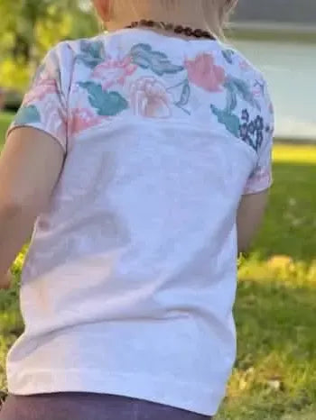 A child from behind wears a cream heather shirt with a floral yoke.