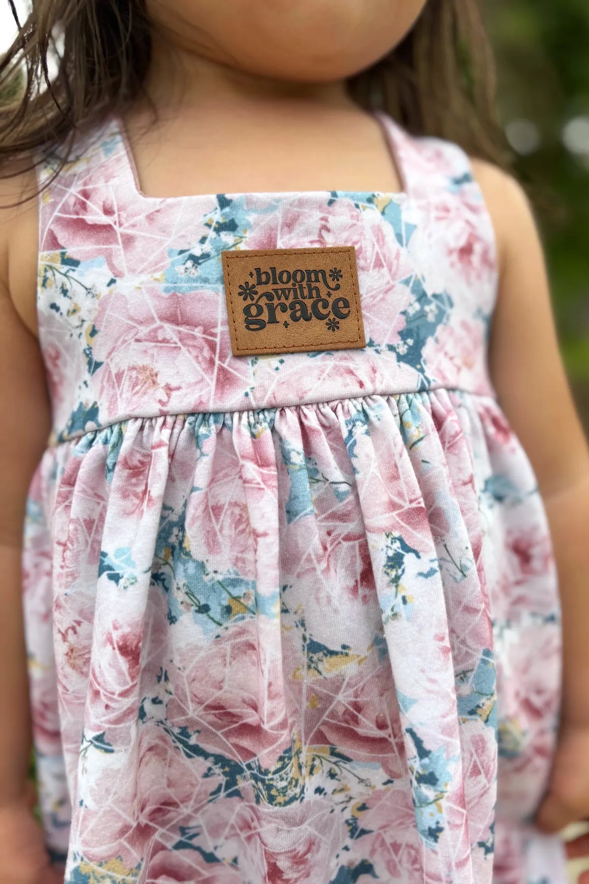 A child wears a floral dress with a "bloom with grace" patch.