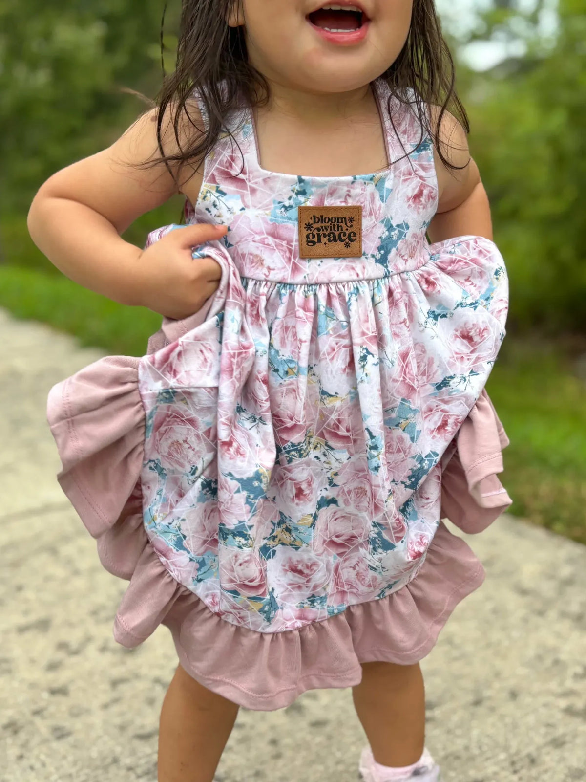 A child in a floral dress with a "bloom with grace" tag.