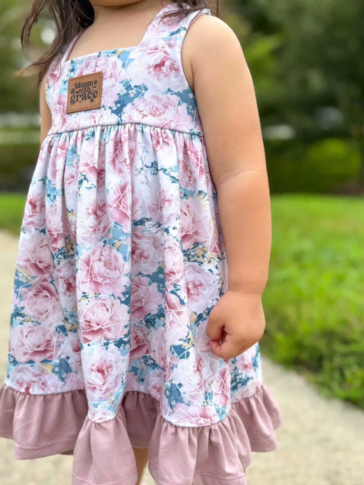 A child wears a floral dress with a "bloom with grace" patch.
