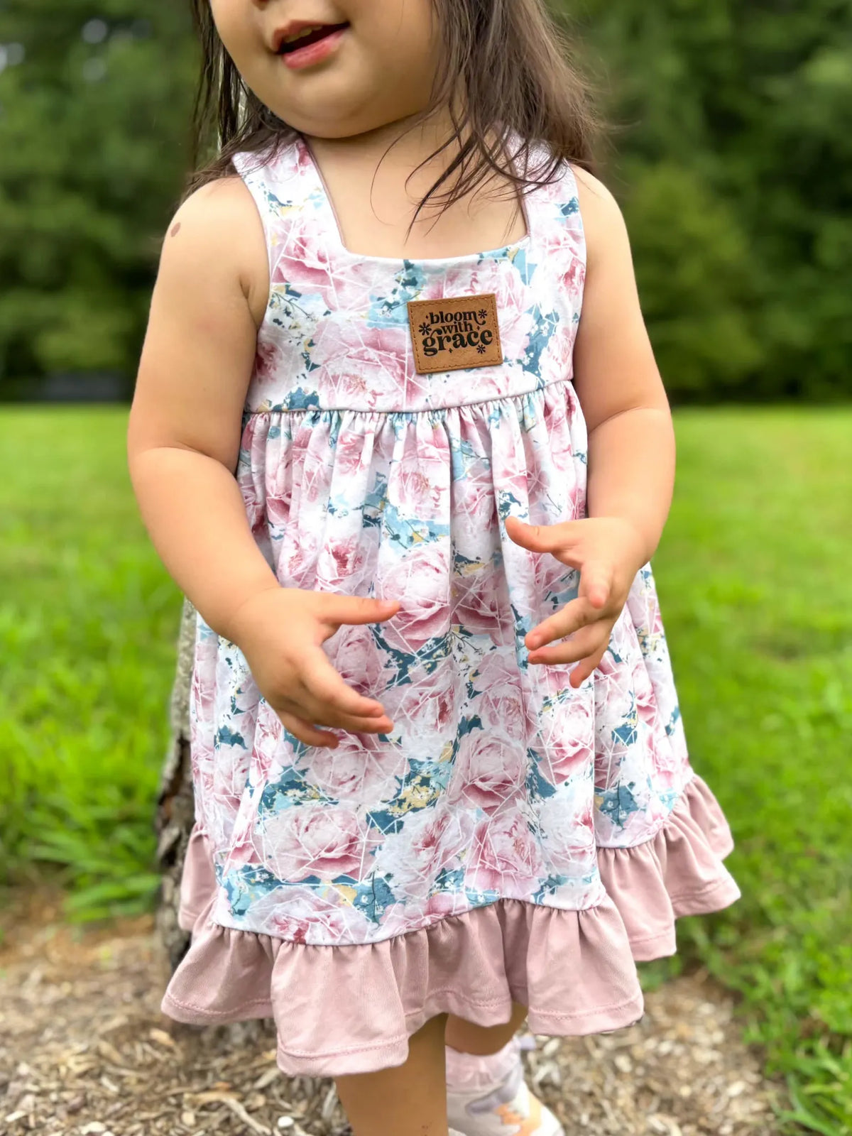 A young child wears a floral dress with a "bloom with grace" patch.