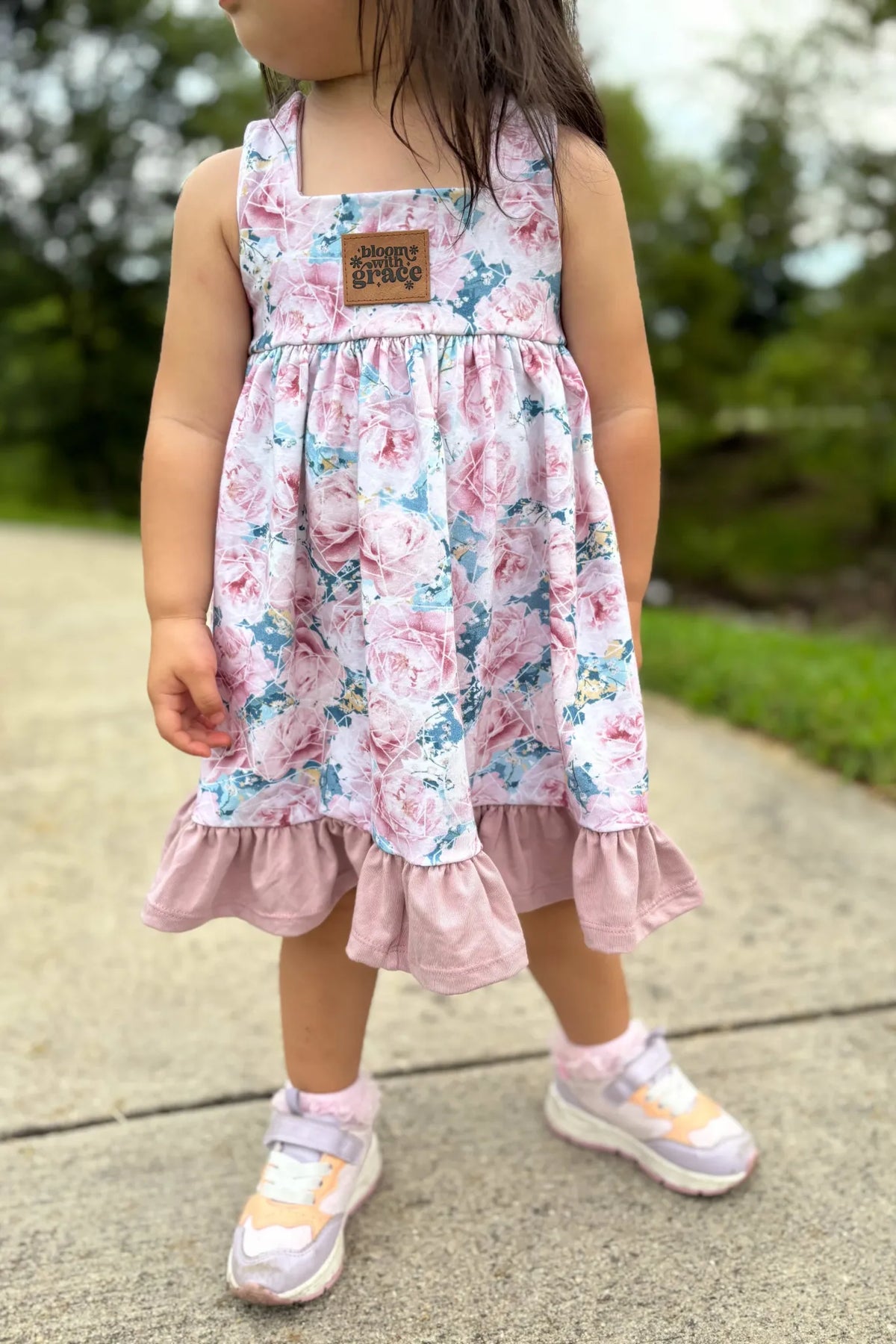 A child in a floral dress with a "bloom with grace" patch and colorful sneakers.
