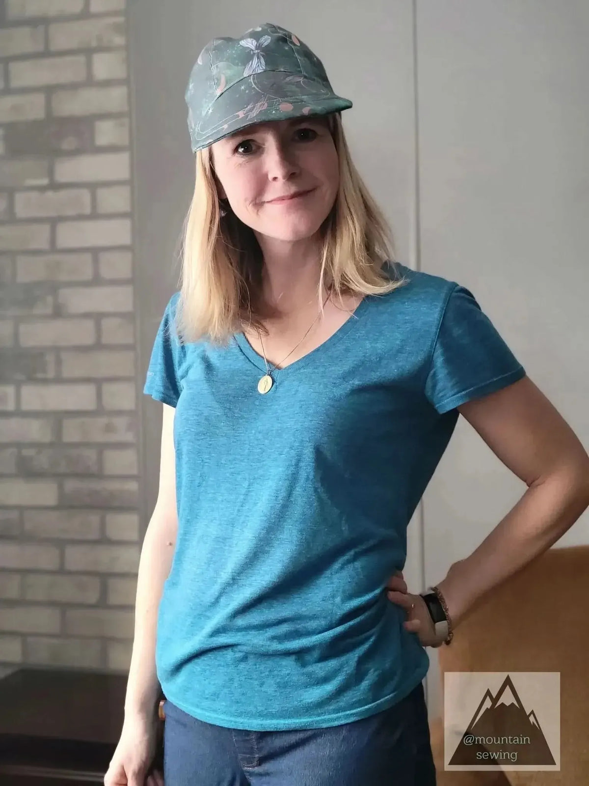 Woman wearing a green cap with celestial dragonflies and a blue v-neck shirt.