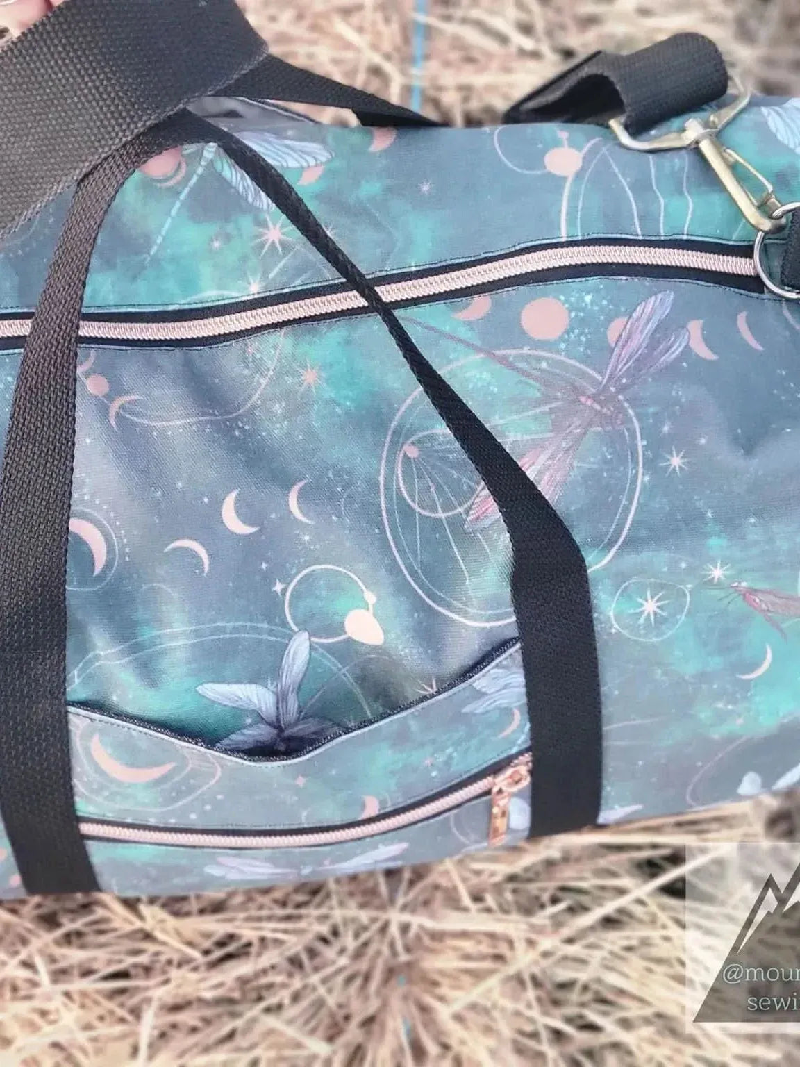 A green duffel bag with a celestial dragonfly pattern and black straps.