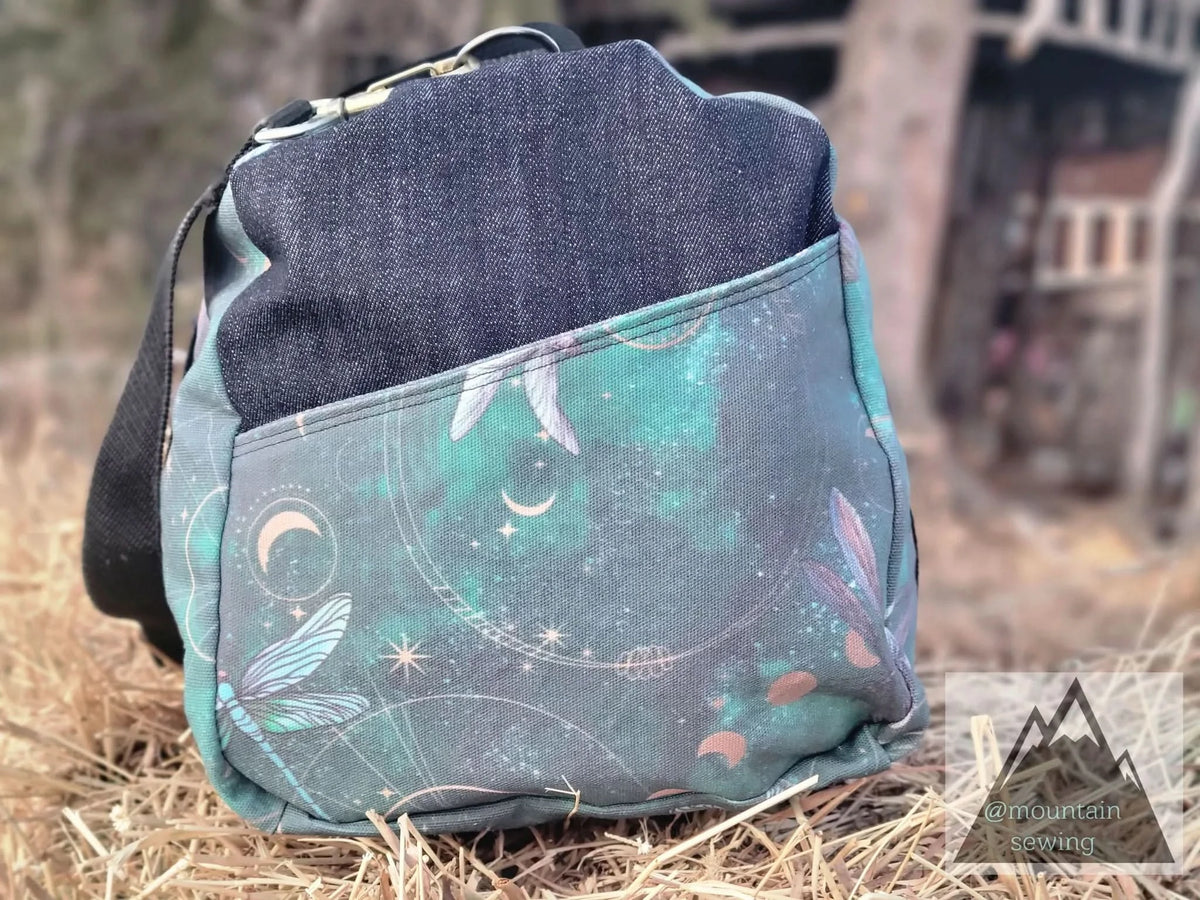 A bag made from Celestial Dragonflies in Green fabric with a denim top and black strap.