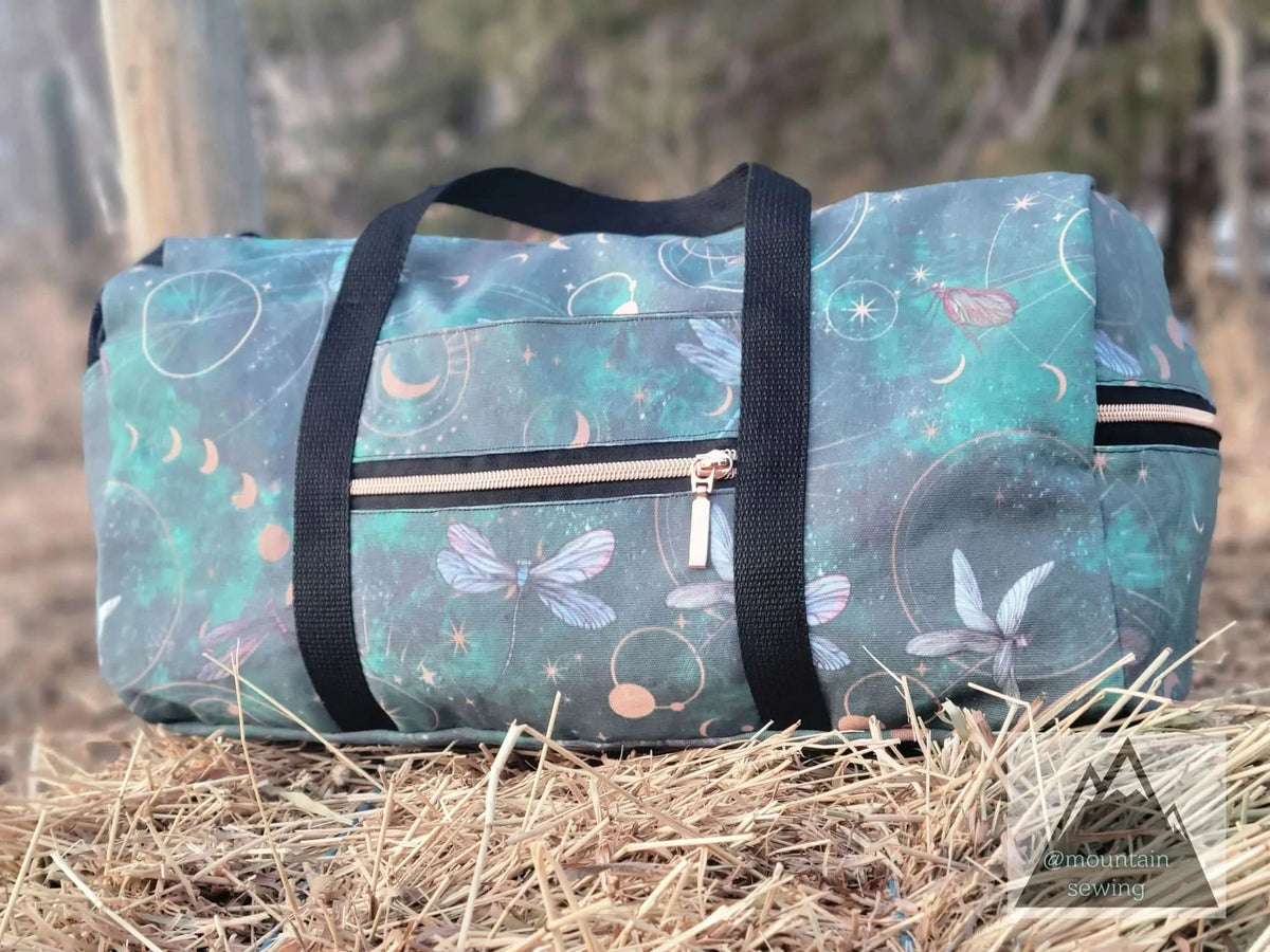 A green duffel bag with celestial dragonfly print and a rose gold zipper.