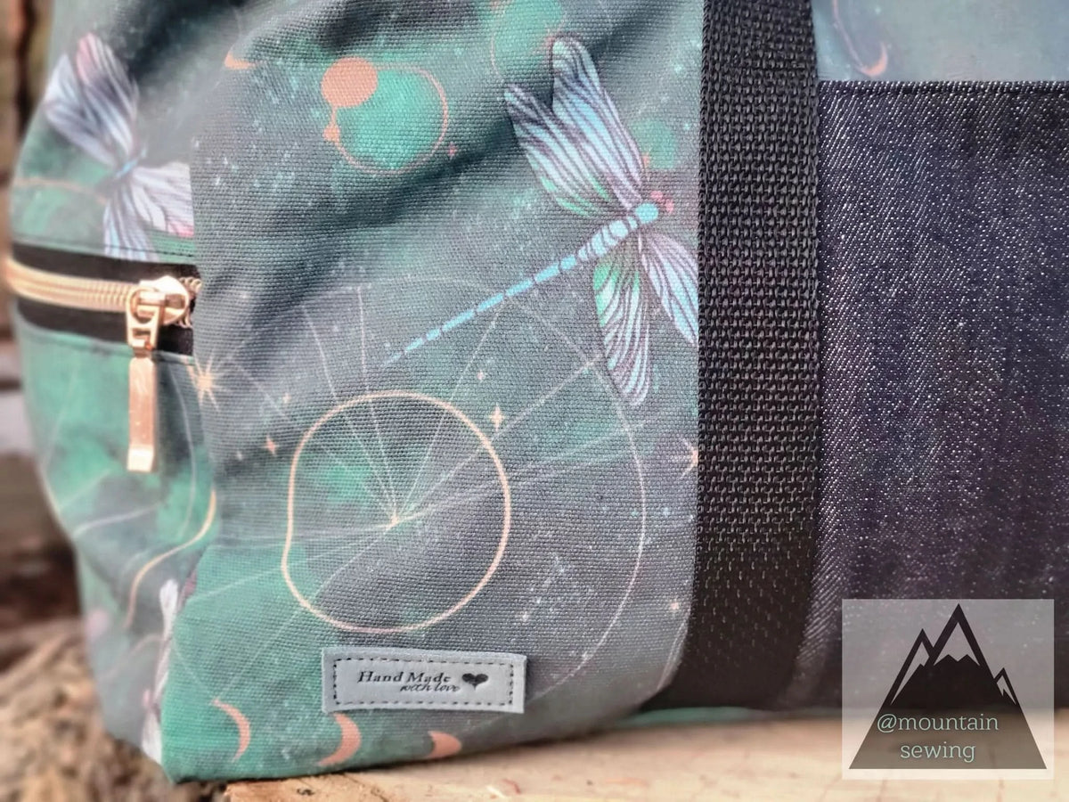 A green bag with celestial dragonflies, a zipper, and a "Hand Made with love" tag.