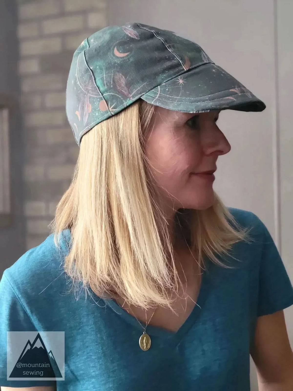 A woman wears a green cap with celestial dragonflies and a blue shirt.