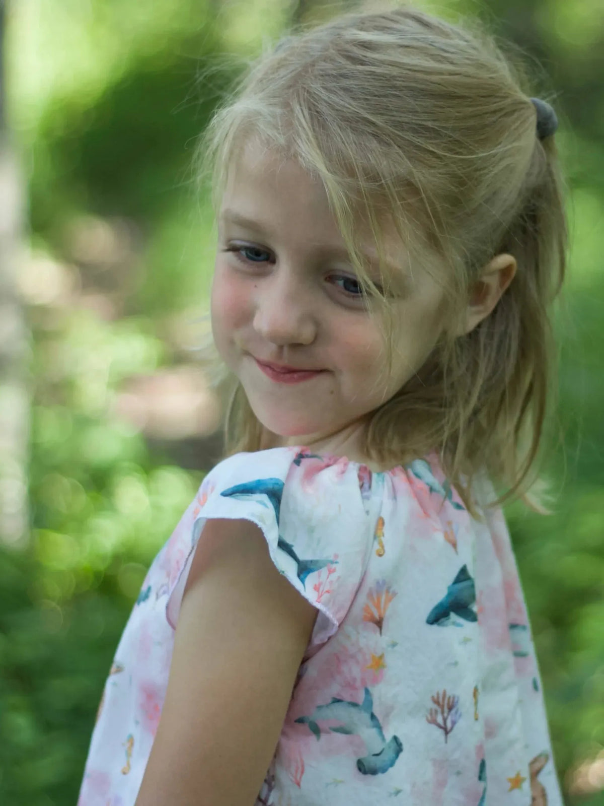 A young girl in a pink "Under The Sea" patterned top smiles, looking over her shoulder.