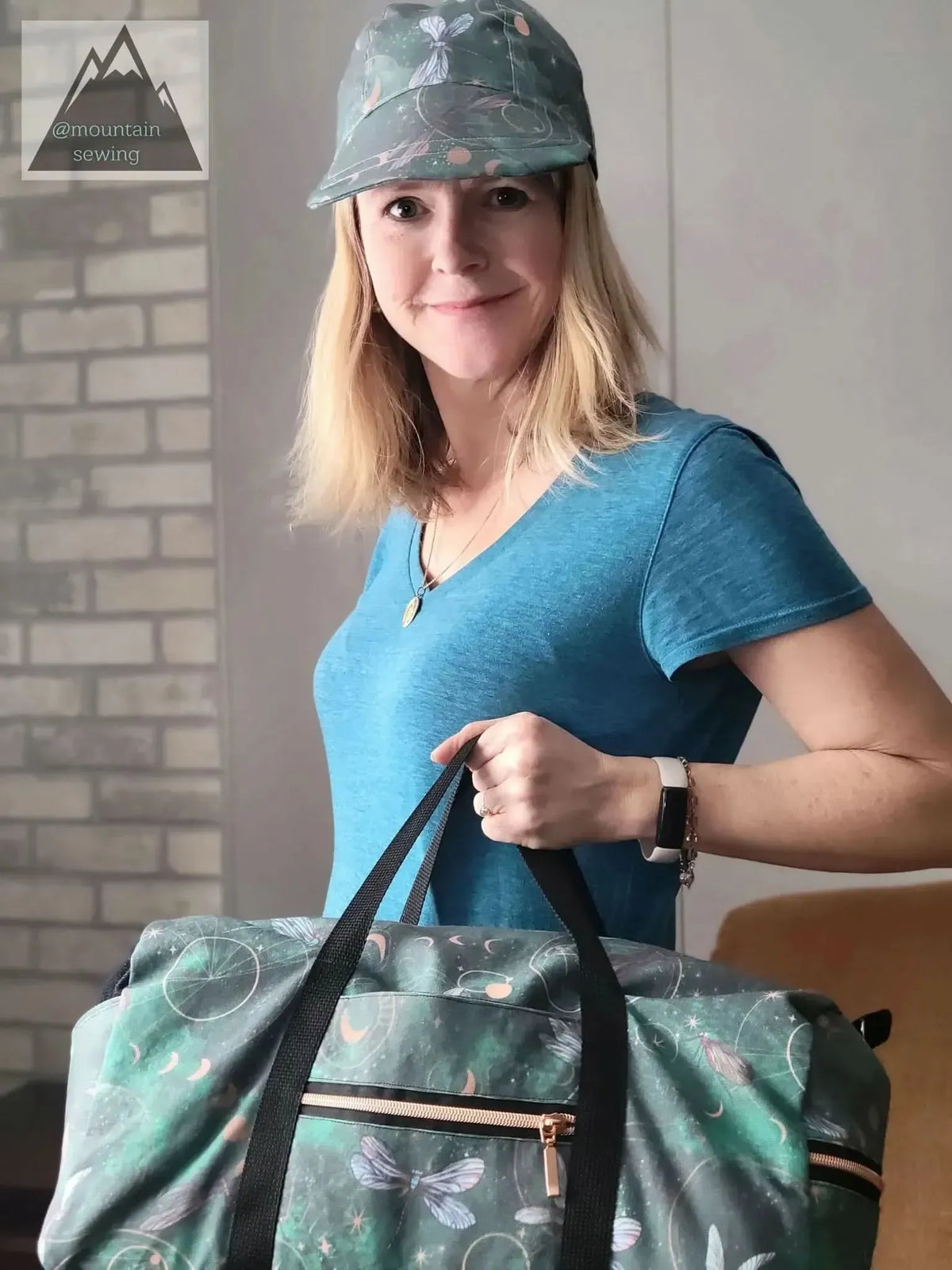 A woman wears a green celestial dragonfly hat and holds a matching duffel bag.