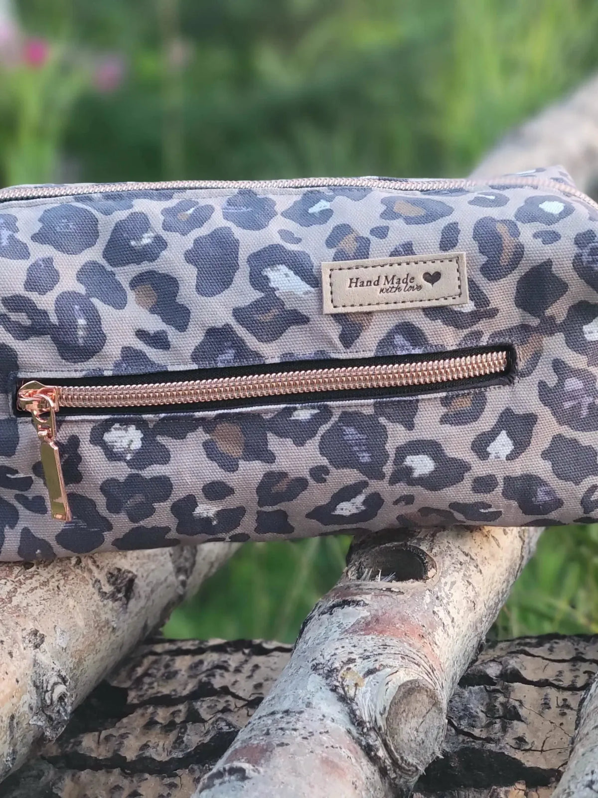 Leopard print pouch with a rose gold zipper resting on tree branches.