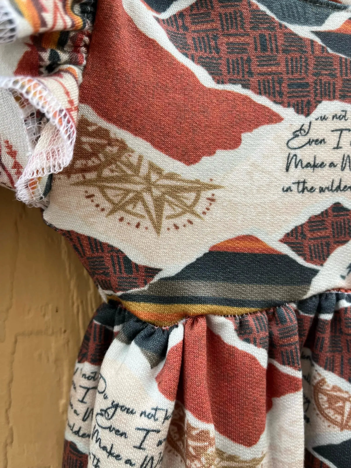Fabric with a compass, mountains, and text in warm tones.