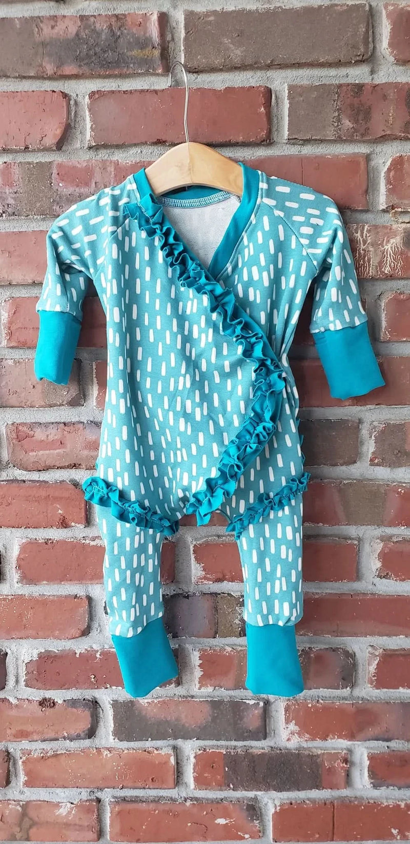 Blue fabric with white dash pattern, made into a baby romper, hanging on a brick wall.