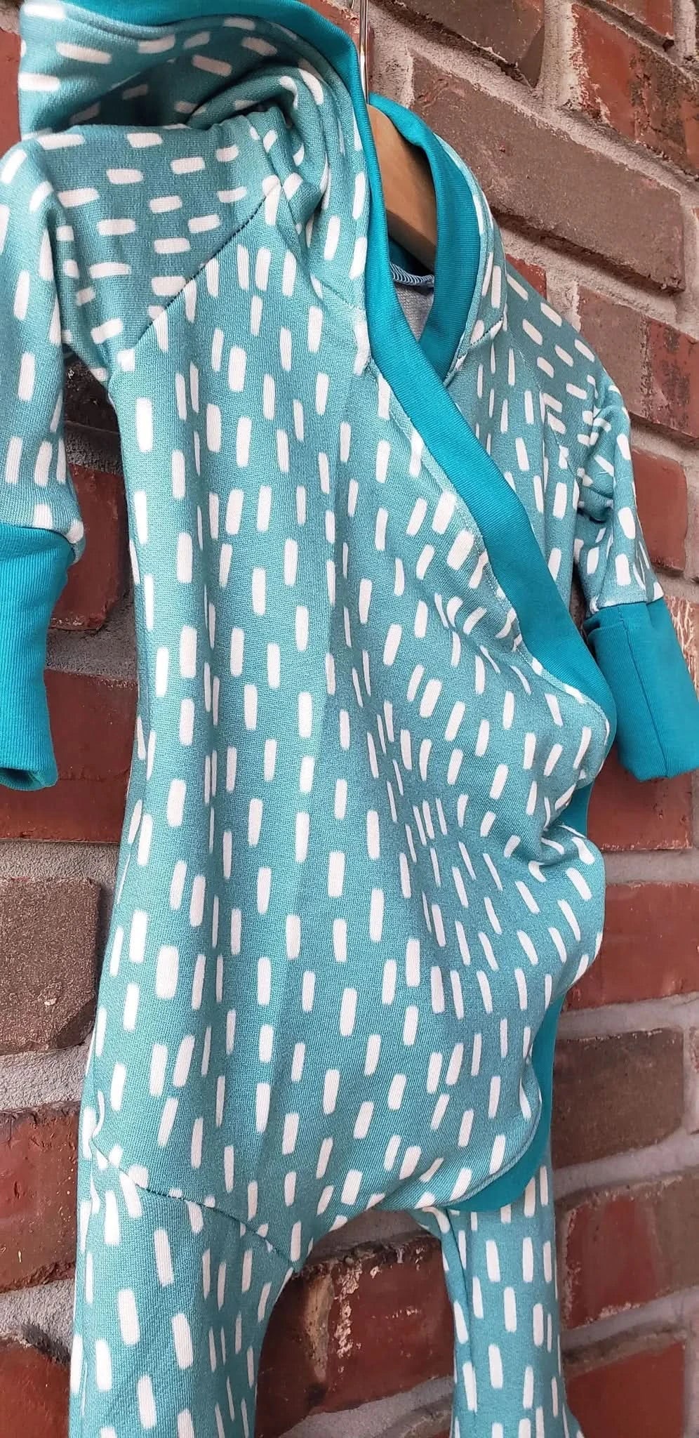 A teal and white patterned baby romper hangs against a brick wall.