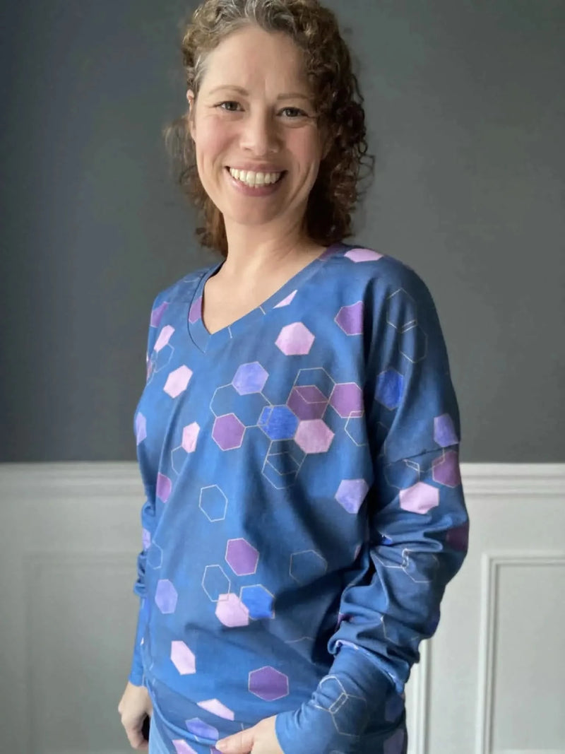 A woman smiles, wearing a blue long-sleeved shirt with purple and blue hexagons.