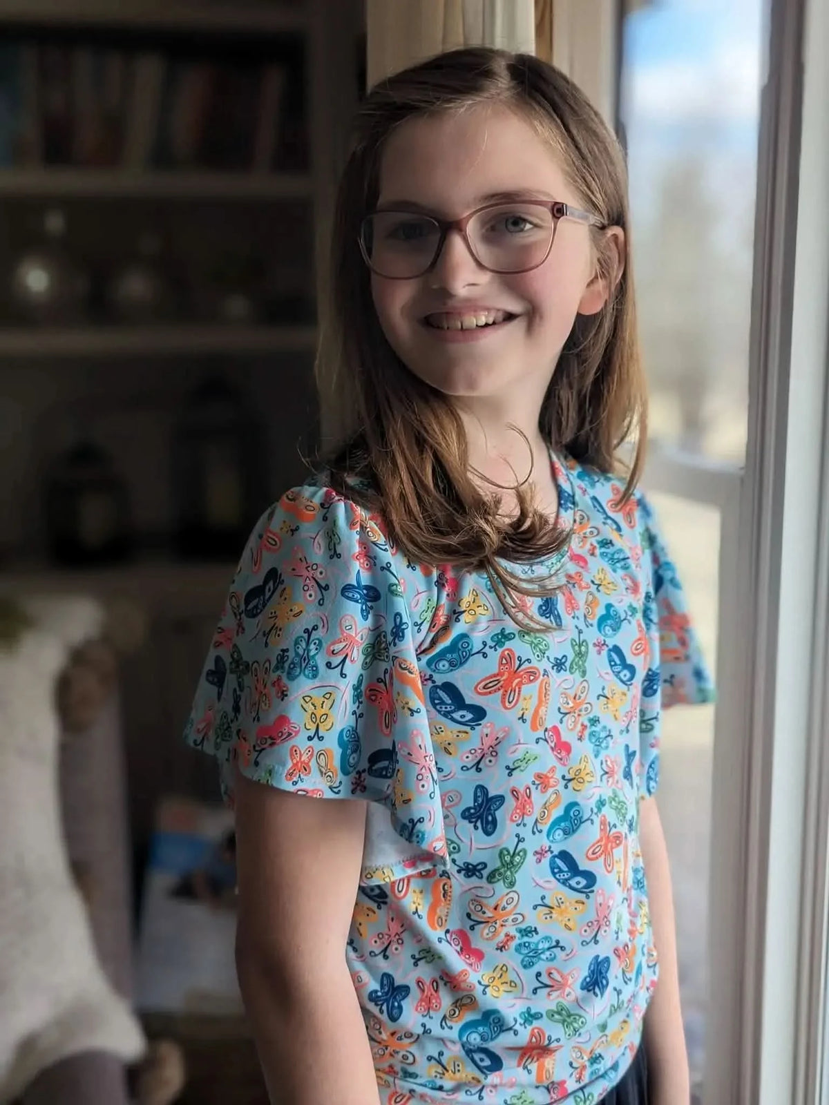 A young girl wears a blue top with a colorful painted butterfly pattern.