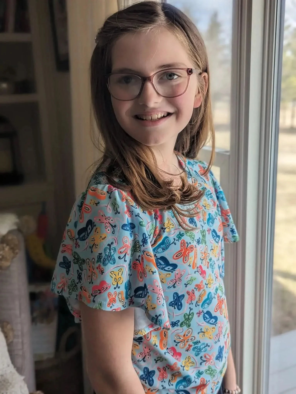 A young girl wearing a light blue shirt with a colorful butterfly pattern.