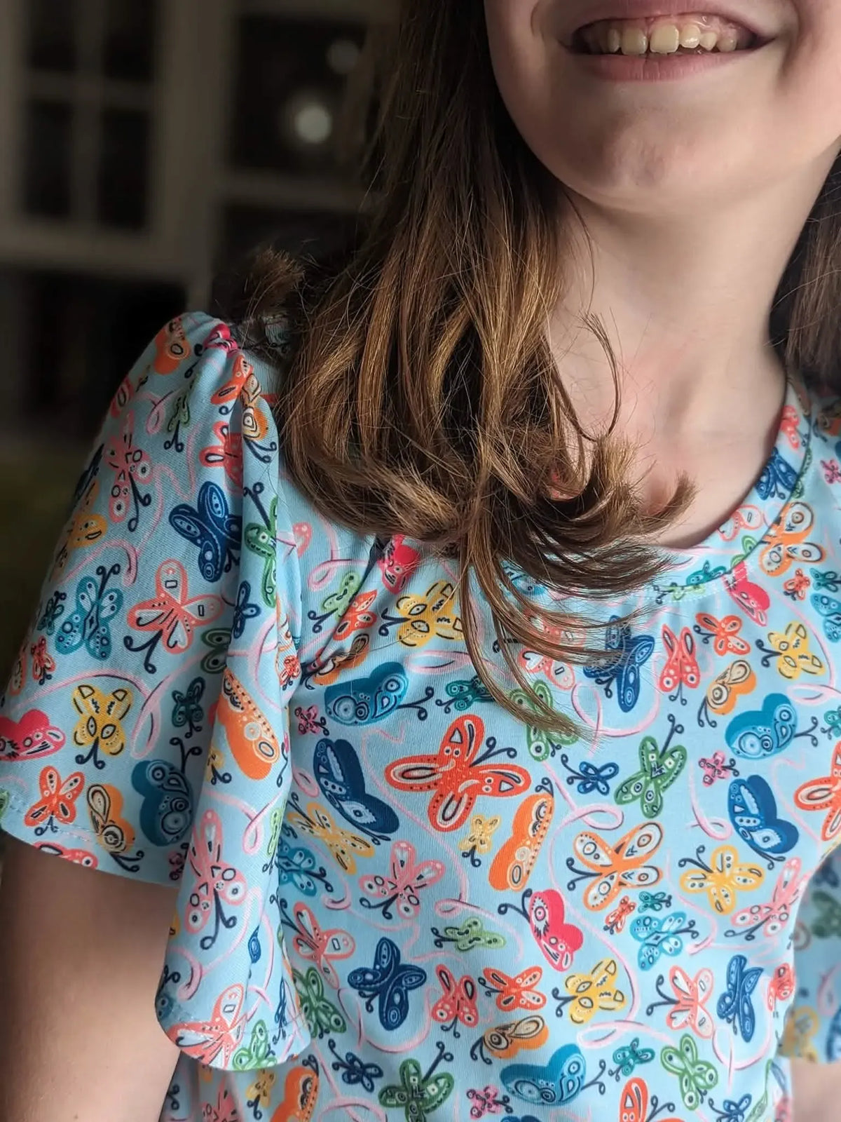 A child wearing a light blue top with a colorful painted butterfly pattern.