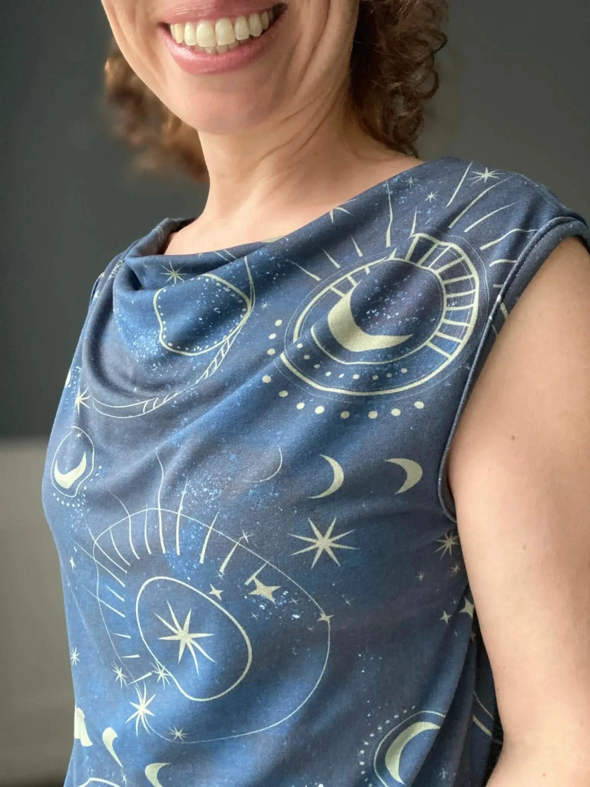 A person smiles while wearing a blue top with a celestial sky pattern.