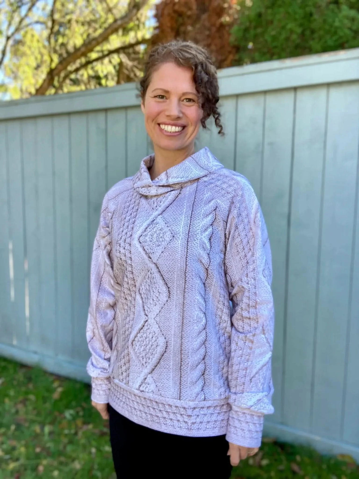 Woman smiling in a cream cable knit cowl neck sweater.