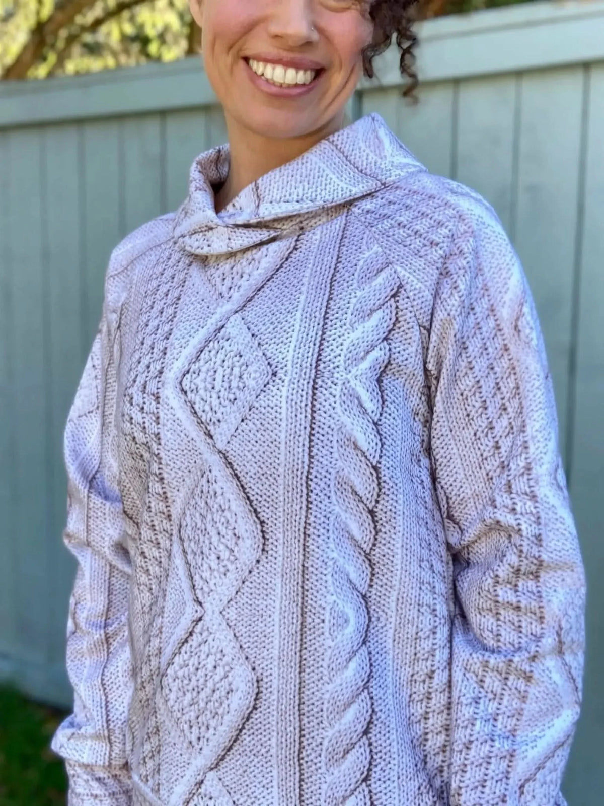A woman smiles while wearing a cream cable knit sweater.