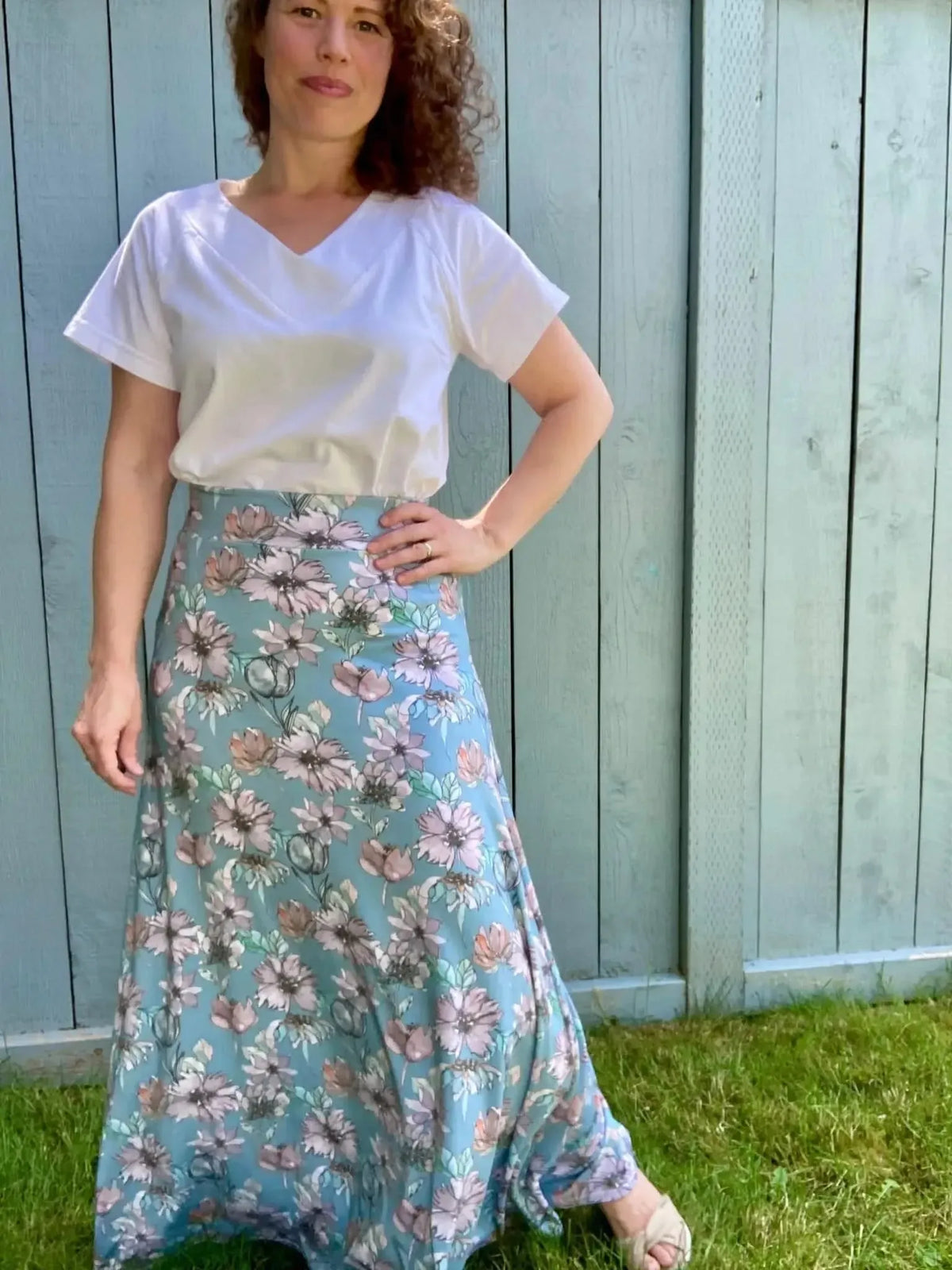 A woman wears a white top and a long floral skirt in shades of blue and pink.