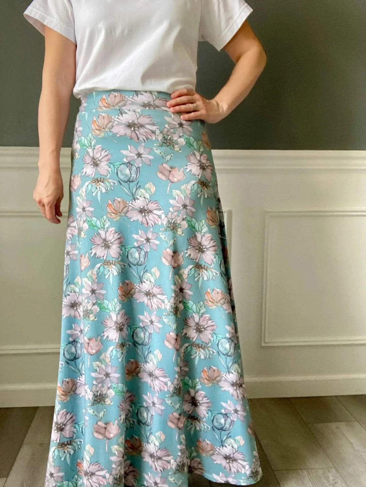 A person wearing a white t-shirt and a long, flowing floral skirt.