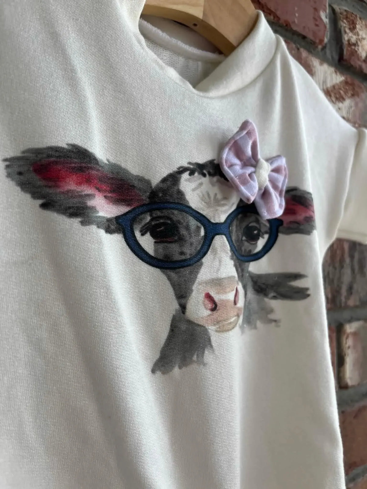 A white fabric panel features a cartoon cow wearing glasses and a pink bow.