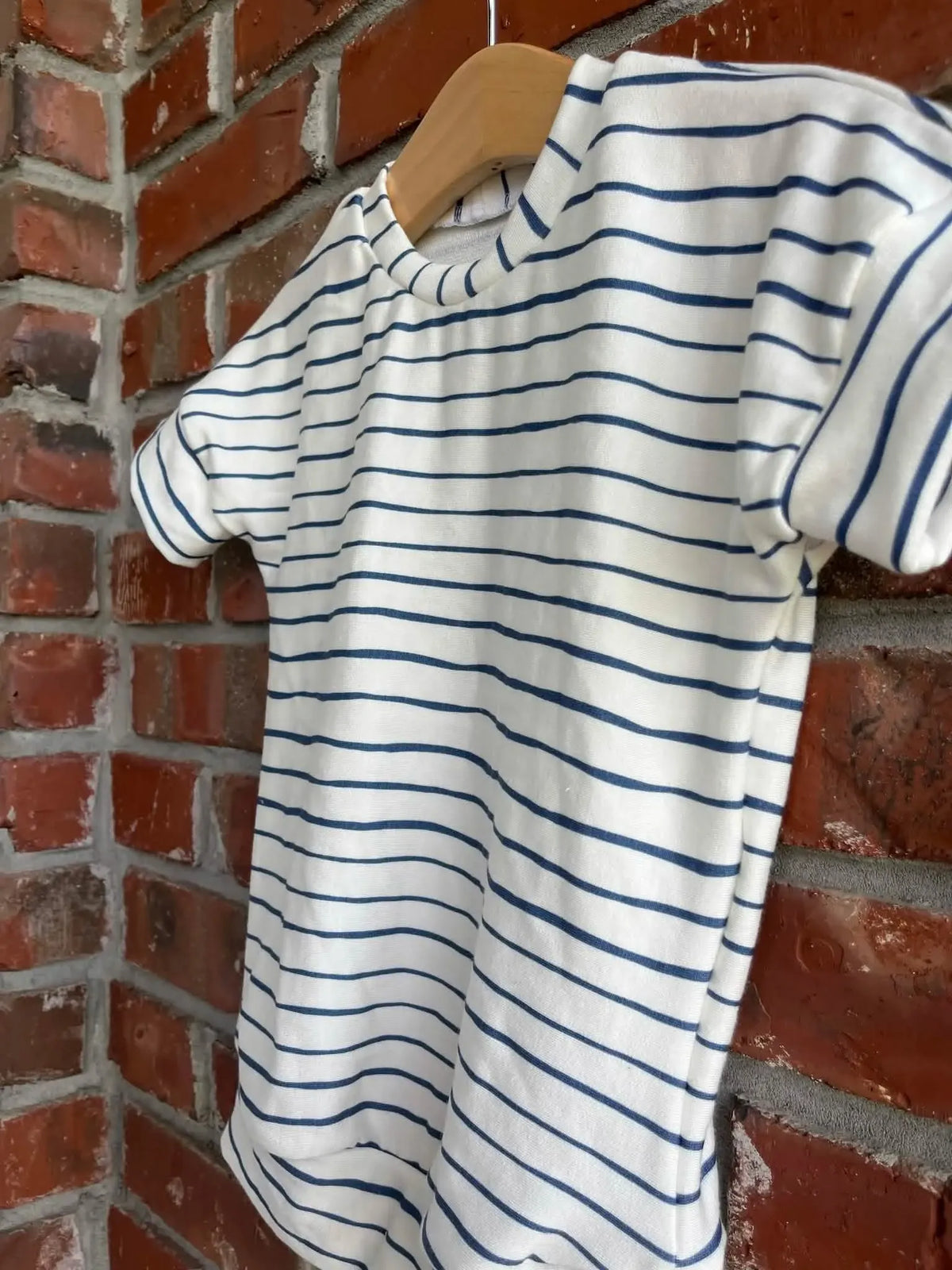 A white t-shirt with navy blue horizontal stripes hangs on a wooden hanger.