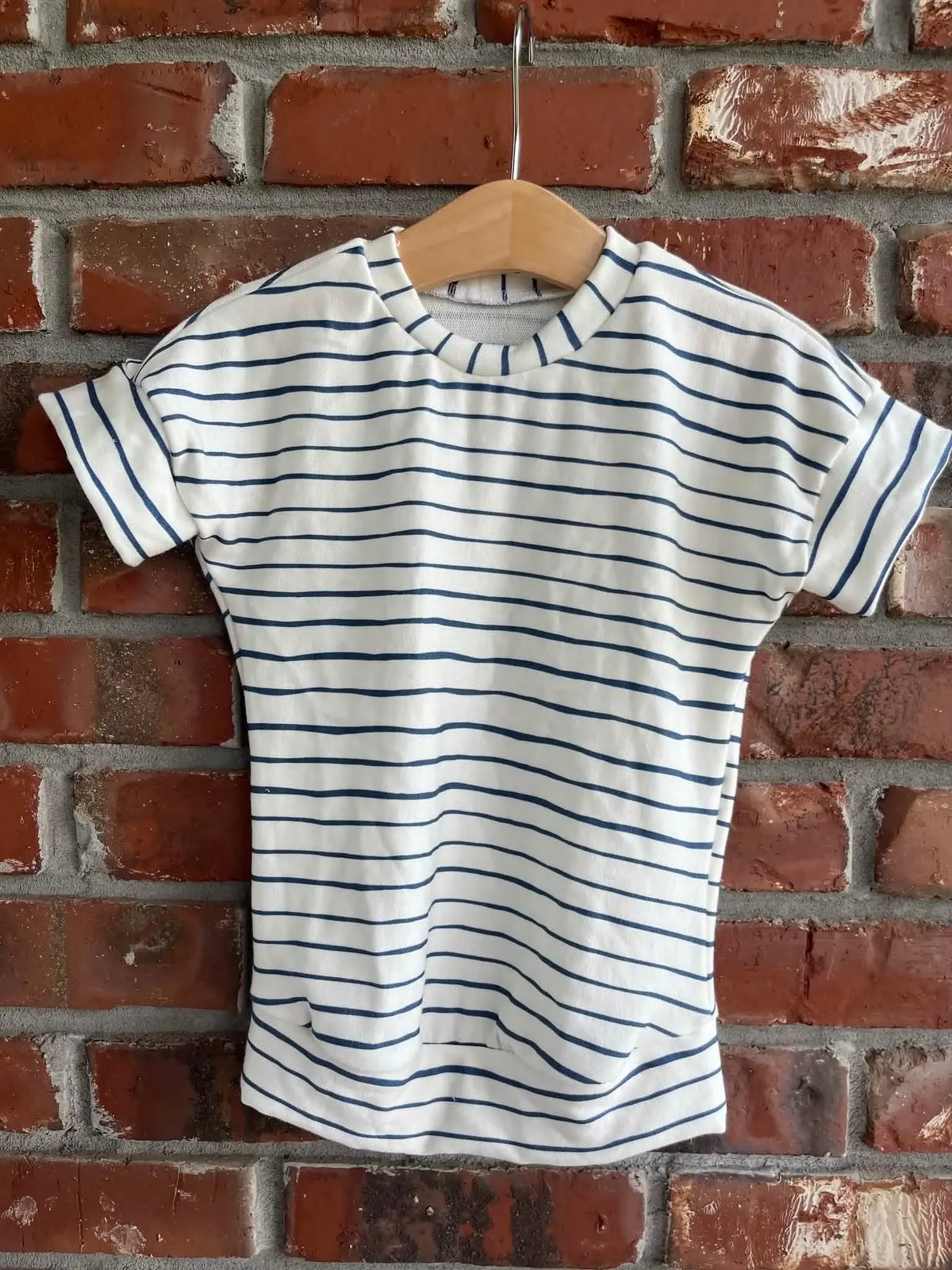 A white t-shirt with navy blue horizontal stripes hangs on a wooden hanger.