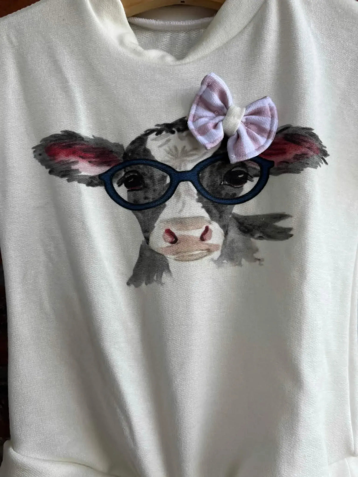 A white fabric panel features a watercolor cow wearing glasses and a pink striped bow.