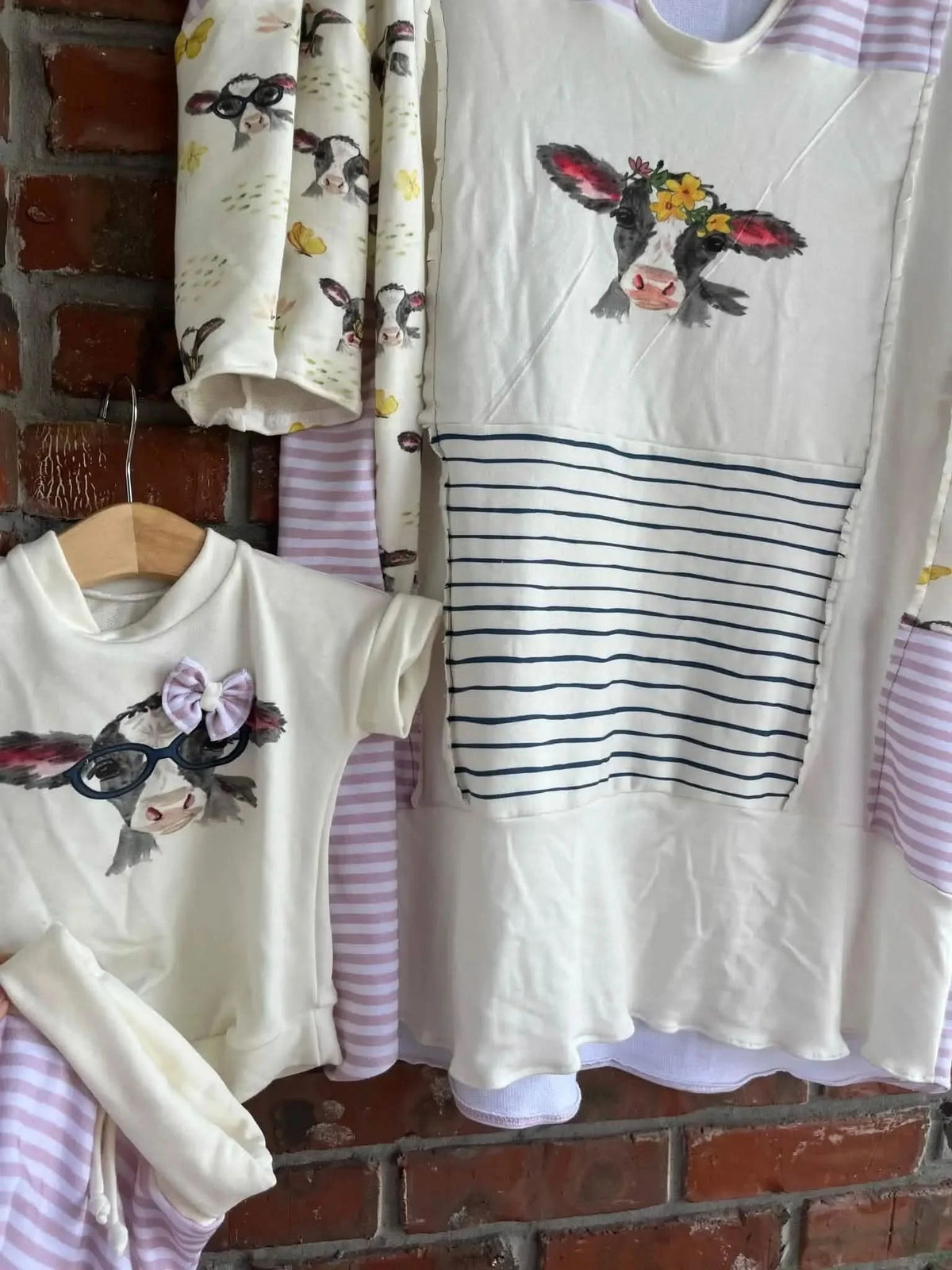 Various garments featuring cow and butterfly prints hang against a brick wall.