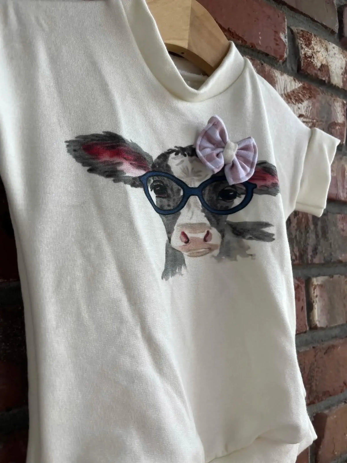 A white fabric panel features a cartoon cow wearing glasses and a pink bow.